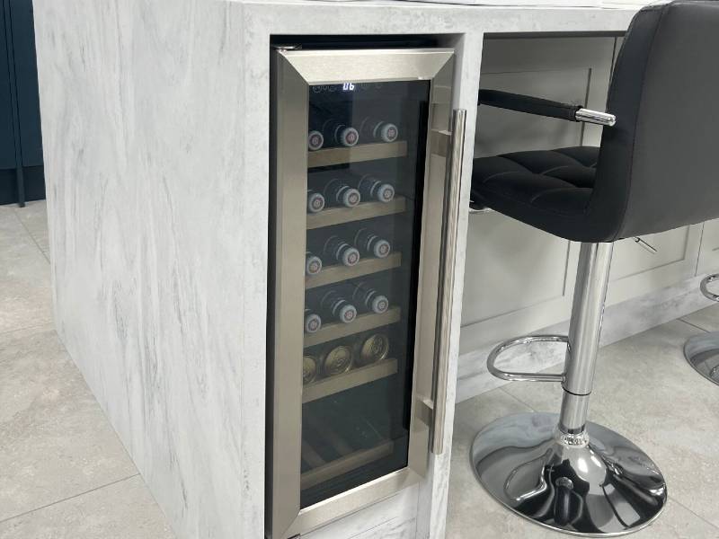 A wine cooler in a kitchen with stools.